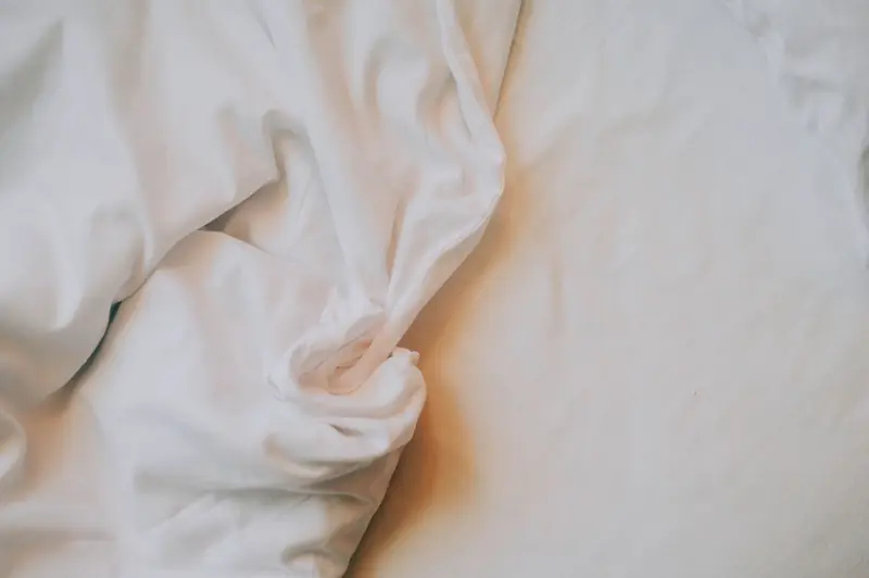 An artistic close-up of crumpled white bed sheets in soft, warm lighting