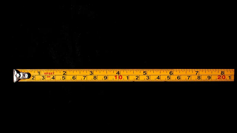 A close-up of a yellow tape measure laid out on a black background