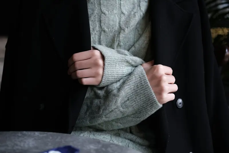Close-up of hands wearing a knitted sweater under a black coat, showcasing winter fashion