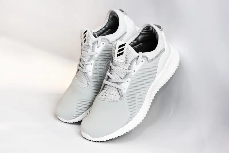Pair of sports shoes with gray dense texture of surface and rubber inserts from sided and laces and white soles placed with heels up leaning on glance gray back