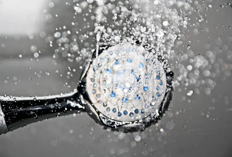 Close-up of a shower head releasing water droplets, creating a crisp and refreshing bathroom scene