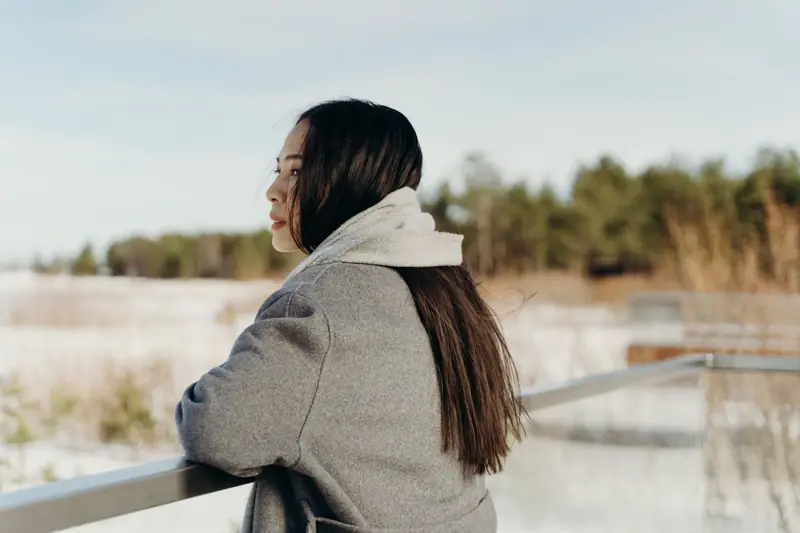 A woman in a warm coat looks out over a snowy landscape, enjoying the serene winter atmosphere