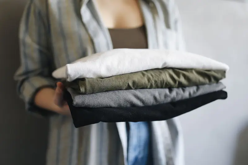 A close-up of a person holding neatly folded shirts, perfect for home organization themes