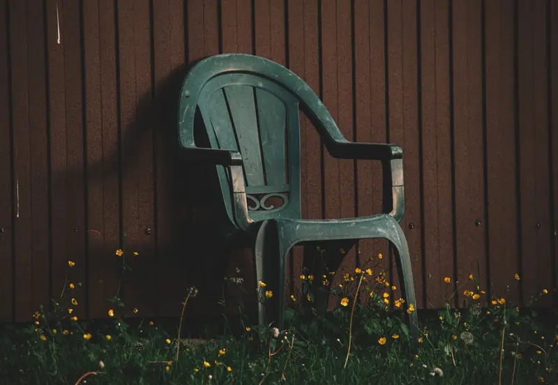 An outdoor plastic chair placed against a wooden wall surrounded by wildflowers in low light