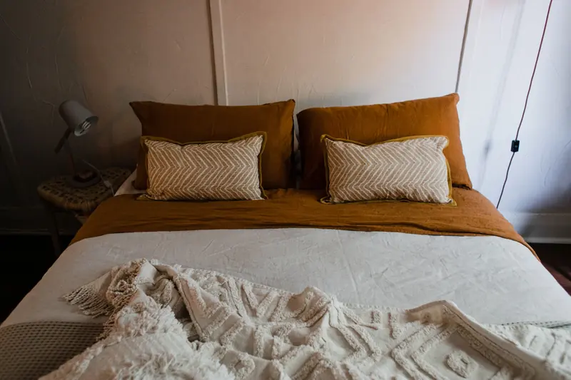 Inviting bedroom with warm tones, featuring a neatly arranged bed, pillows, and ambient lighting