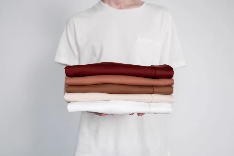 Minimalist close-up of folded neutral-colored shirts held by a person