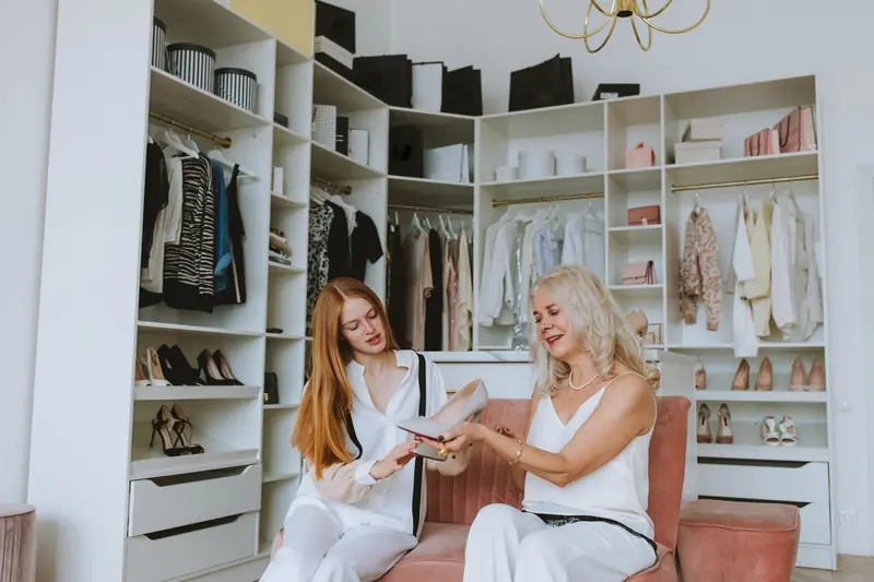 Two women in a stylish walk-in closet discussing and examining shoes
